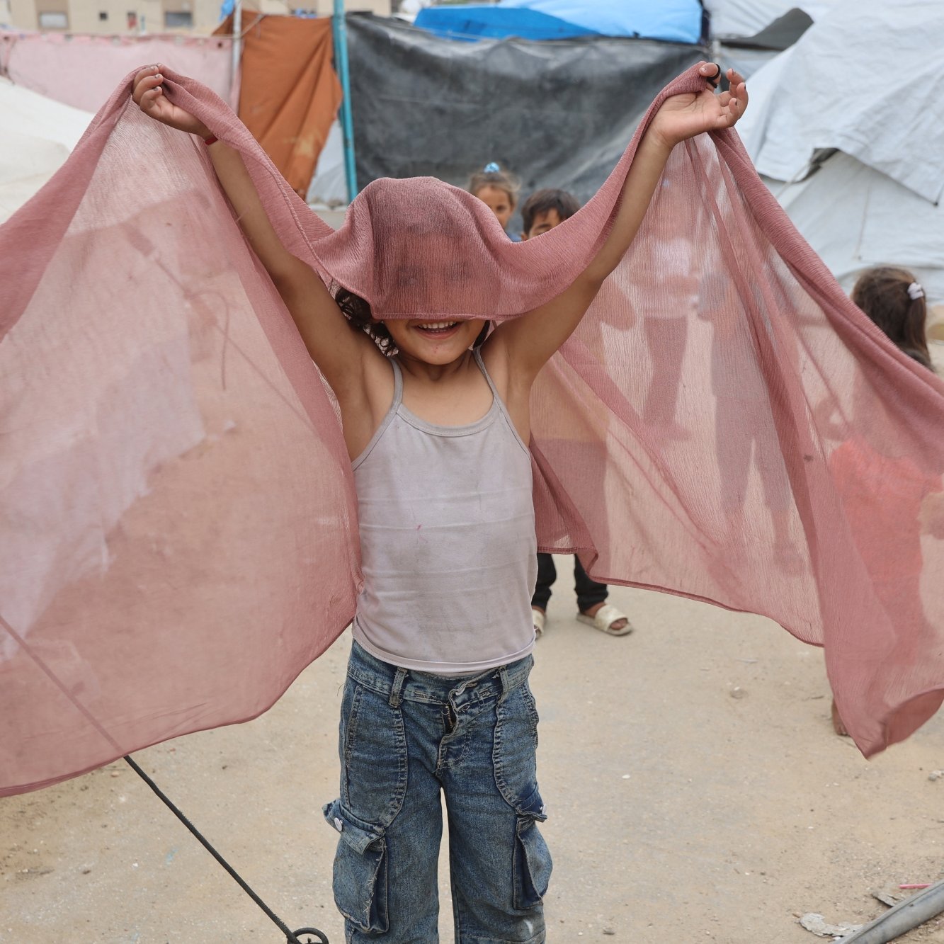Enfant joyeux tenant un tissu léger, jouant près de tentes.