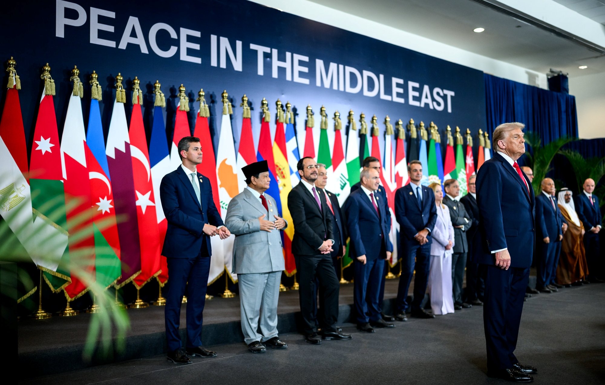 A group of leaders stands in front of flags, with one man speaking, promoting Middle East peace.