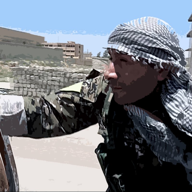 The image shows a soldier or combatant wearing a camouflage uniform and a traditional scarf, possibly indicating a specific cultural or regional background. The individual appears to be in an urban or semi-urban setting, with buildings and debris in the background. The person is depicted in a moment of alertness or movement, suggesting a context related to military operations or conflict. The environment looks tense and potentially dangerous.