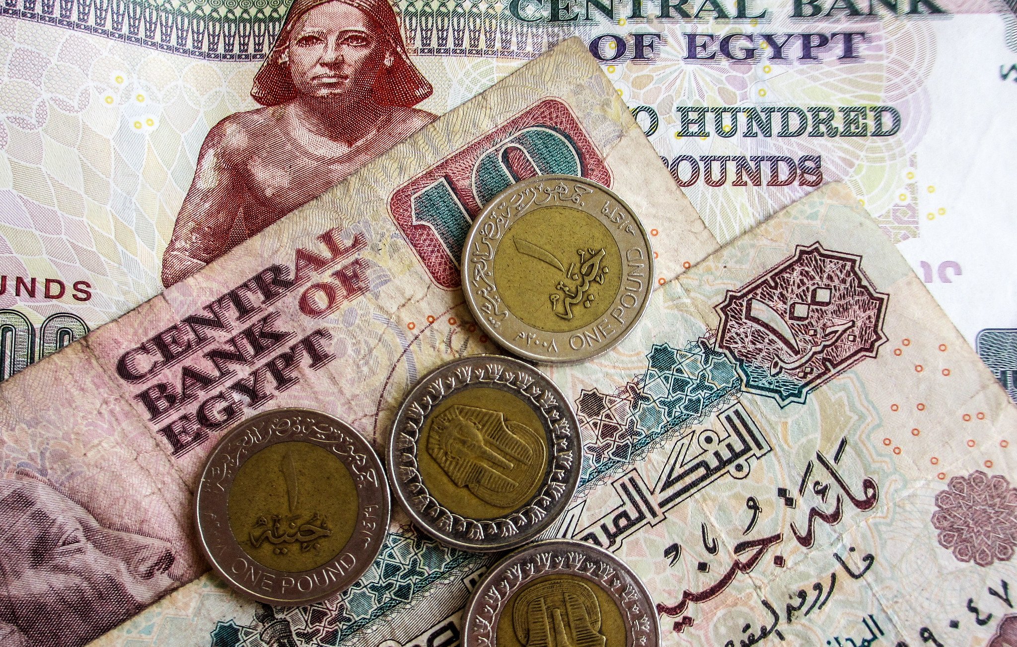 در این تصویر، تعدادی پول نقد مصری به نمایش گذاشته شده است. شامل یک اسکناس ۲۰۰ پوندی و یک اسکناس ۱۰ پوندی که در پس‌زمینه دیده می‌شود. همچنین چهار سکه یک پوندی روی اسکناس‌ها قرار دارد. طراحی اسکناس‌ها و سکه‌ها حاوی نقوش و نوشته‌هایی به زبان عربی است که بیانگر هویت بانک مرکزی مصر و ارزش پول‌ها می‌باشد. رنگ‌های مختلف اسکناس‌ها و سکه‌ها به وضوح قابل مشاهده است.
