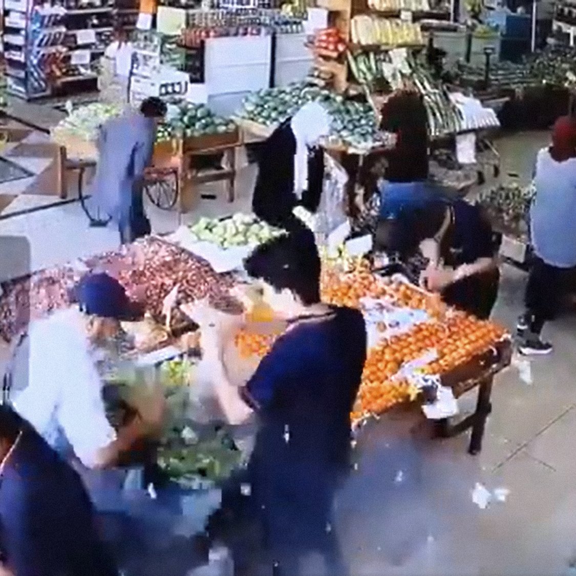 تظهر في الصورة مشهدًا من داخل سوق لبيع الفواكه والخضروات. يبدو أن هناك عددًا من الأشخاص يتواجدون في السوق، حيث يقوم البعض بتفقد المنتجات بينما الآخرون مشغولون بترتيبها أو شراءها. الألوان زاهية، مع الكثير من الفواكه والخضروات المعروضة على الطاولات، مما يعطي انطباعًا بالنشاط والحيوية في المكان. كما أن الإضاءة جيدة، مما يسهل رؤية التفاصيل.