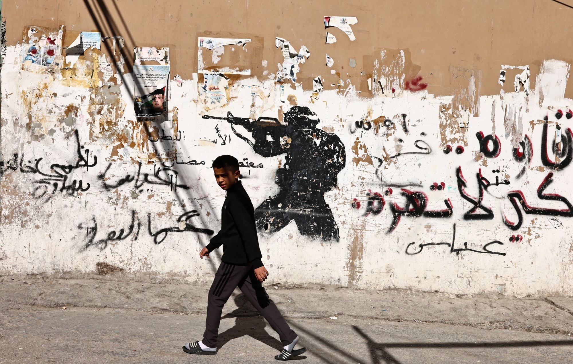 Un garçon marche devant un mur graffiti avec une silhouette de soldat.