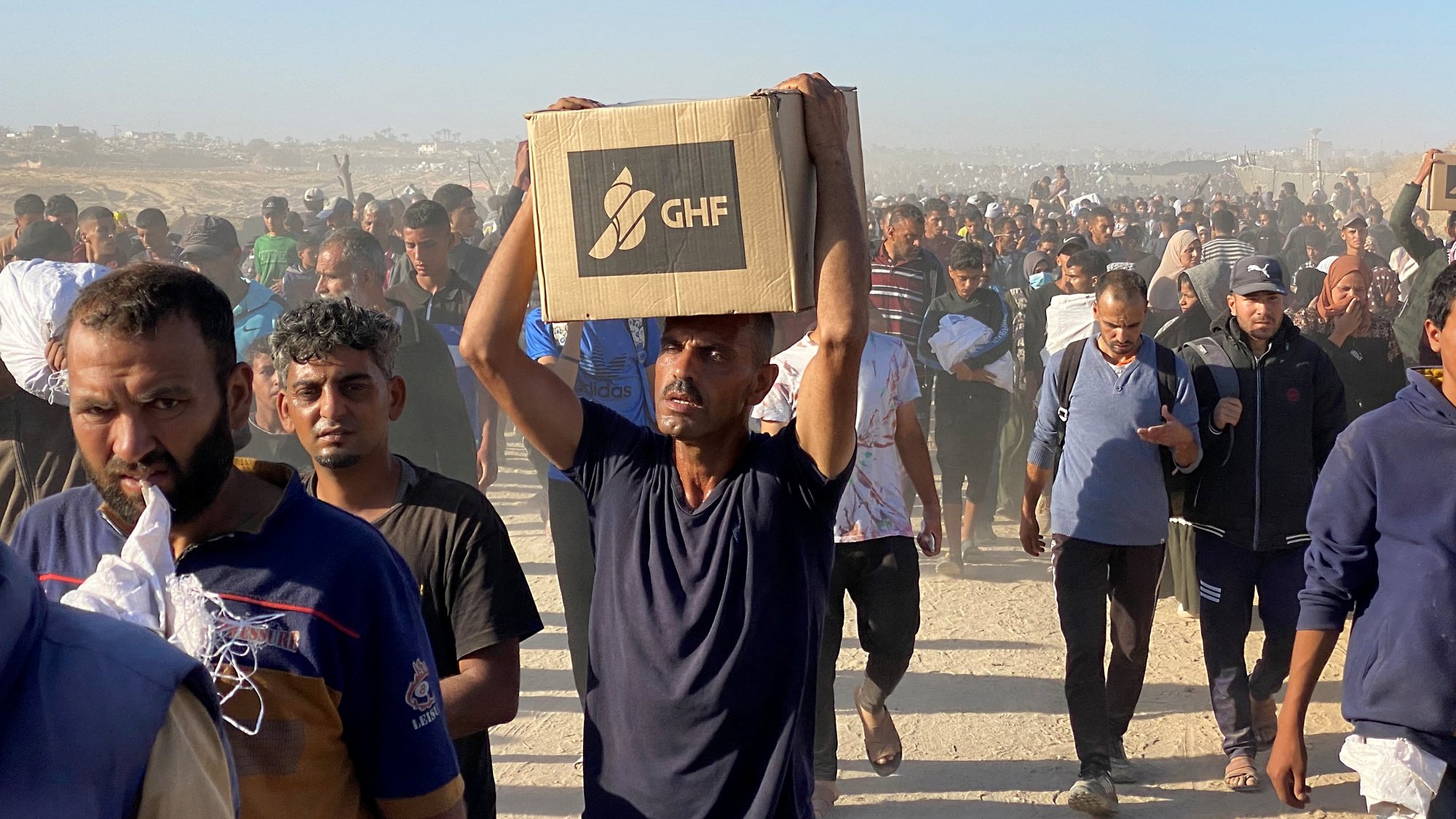 Un gruppo di persone cammina in un ambiente polveroso, portando scatole.