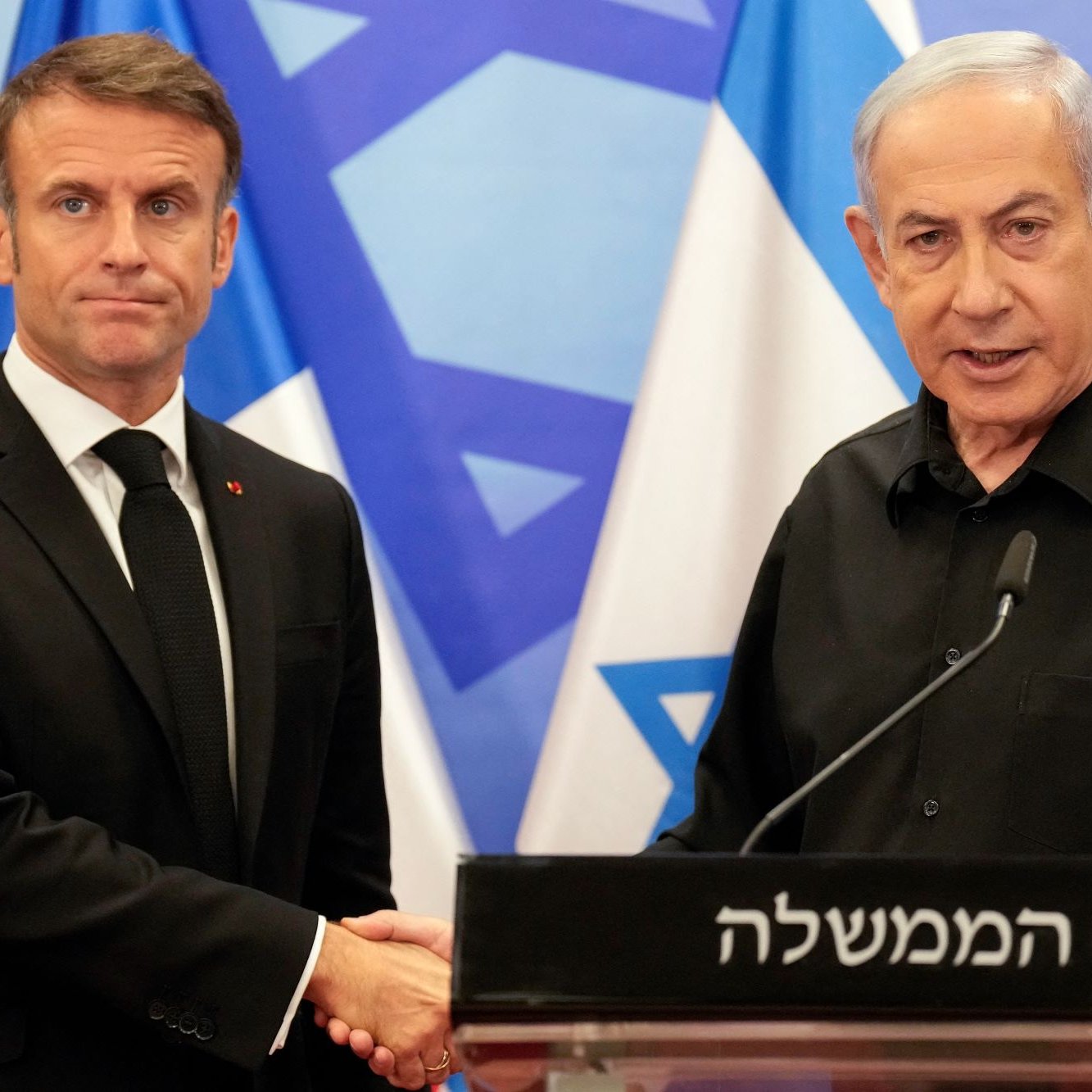 تظهر الصورة اثنين من الرجال أثناء مصافحة، حيث يقف أحدهما على اليمين وهو يرتدي ملابس سوداء، بينما الآخر يرتدي بدلة سوداء طويلة الأكمام. خلفهم تظهر أعلام، يبدو أنها تعود لدولة إسرائيل. تدل تعابير وجوههم على جدية اللقاء، ومن الواضح أنه حدث رسمي.