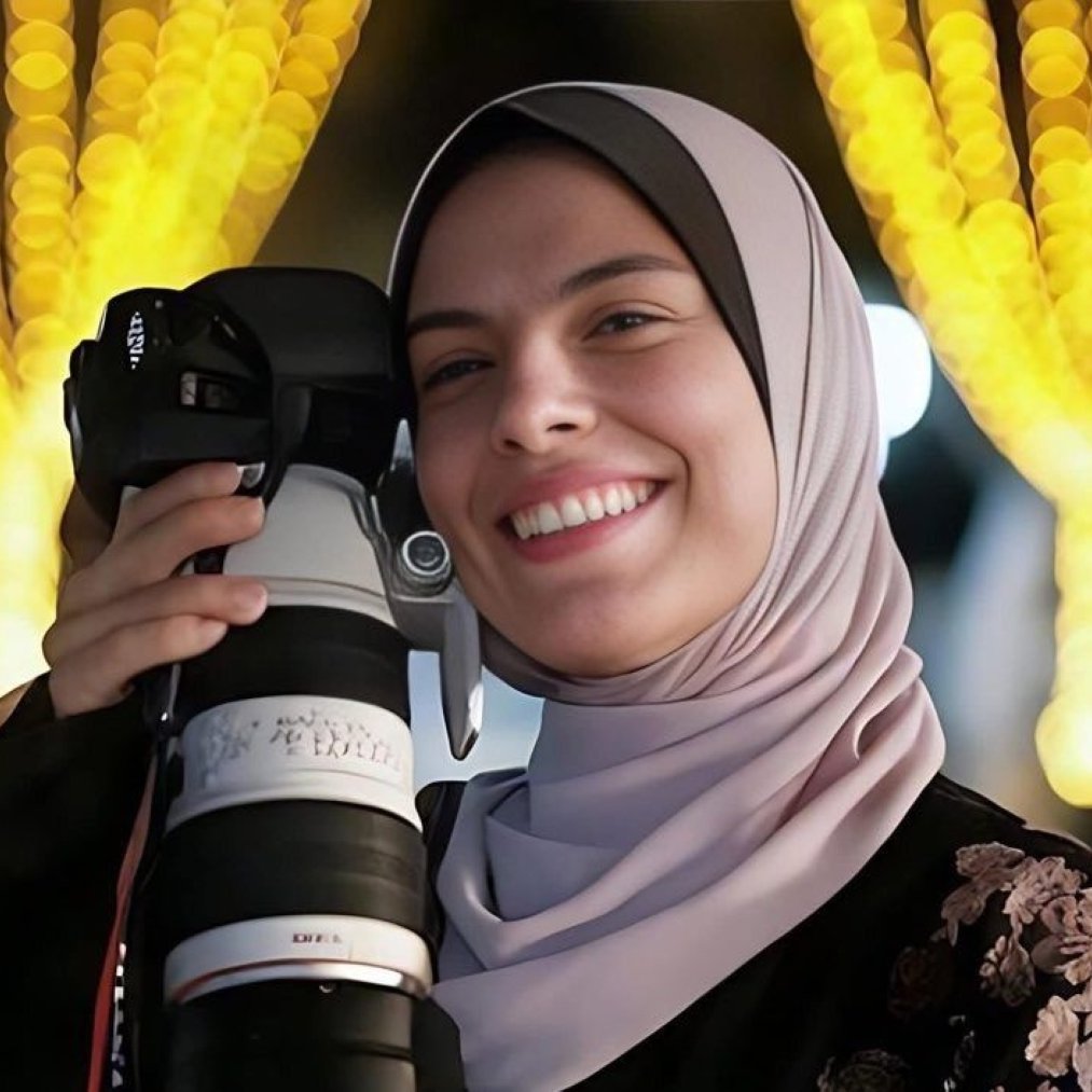 Jeune femme souriante avec un appareil photo, entourée de lumières scintillantes.