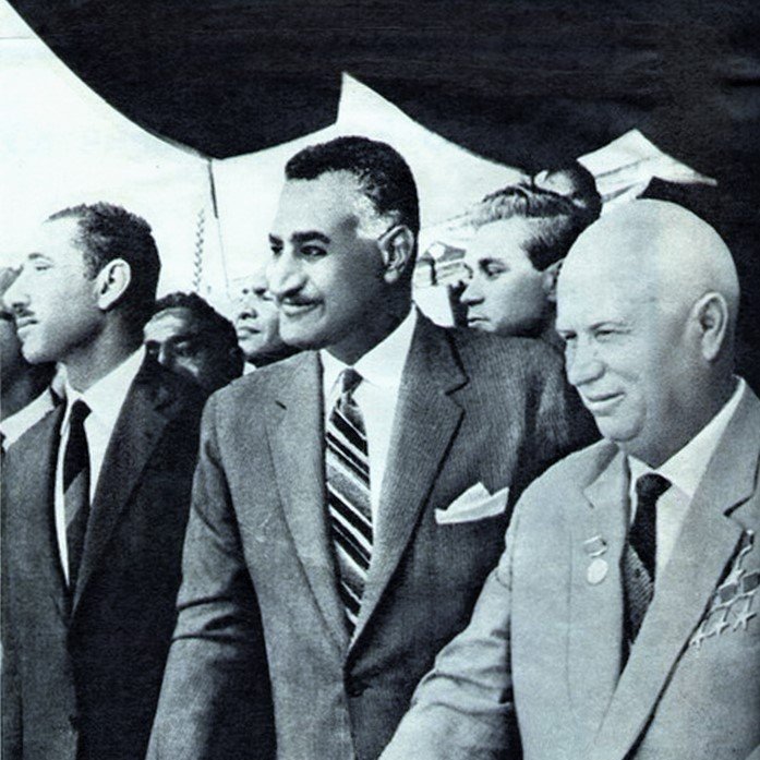 الصورة تظهر ثلاثة رجال يقفون في حدث رسمي. الرجل في المنتصف يرتدي بدلة أنيقة مع ربطة عنق، ويظهر عليه مظهرٌ واثق. الشخصان الآخران على جانبيه يبدو أنهم يرتدون ملابس رسمية أيضًا. يبدو أن البيئة من حولهم تشير إلى مناسبة مهمة. للحظة، يبدو أنهم يتحدثون أو يتبادلون الآراء حول موضوع ما. الصورة تحمل طابعًا تاريخيًا، ربما تشير إلى فترة معينة في السياسة أو العلاقات الدولية.