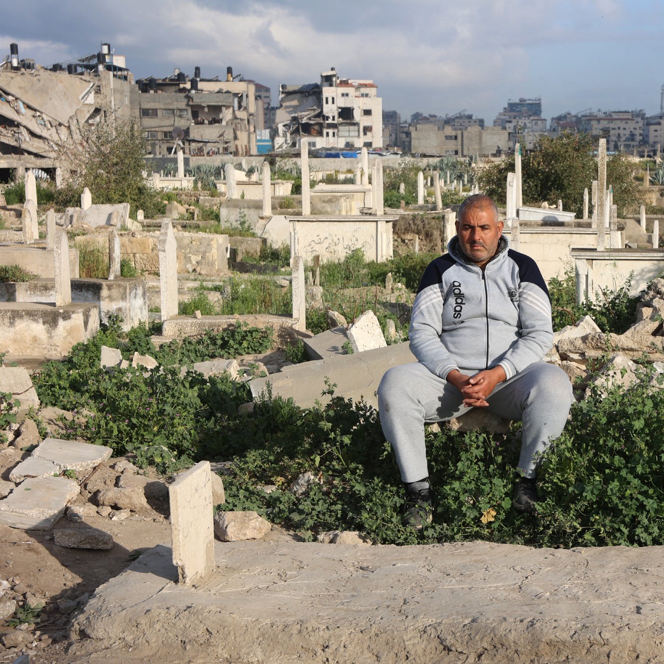 Un homme assis parmi des tombes dans un cimetière, entouré de végétation.
