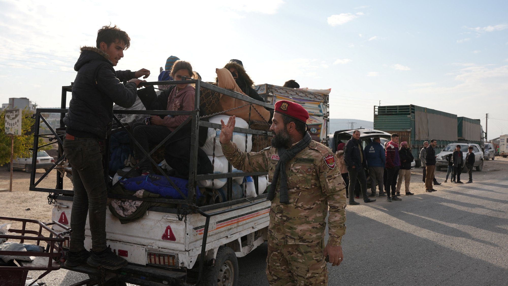 Des personnes sur une camionnette, un soldat gesticule au sol. Atmosphère tendue.