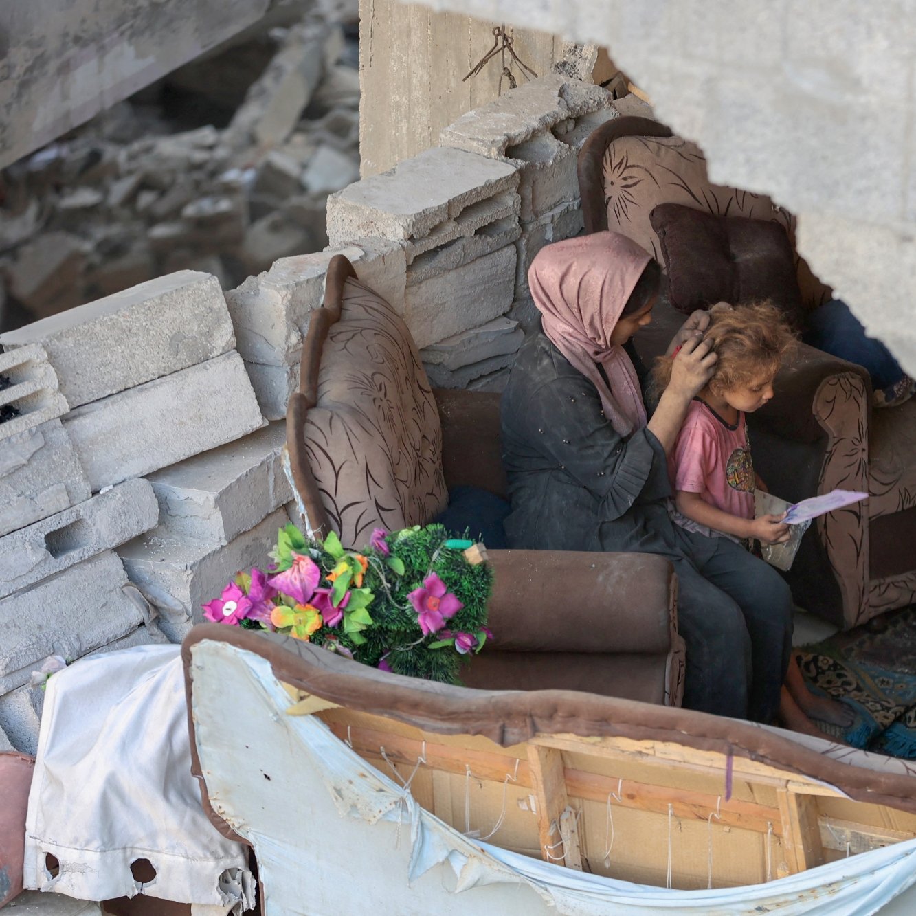 مادری بر روی مبل خراب نشسته و موهای کودک را نوازش می‌کند. در پس‌زمینه، ویرانی مشهود است.