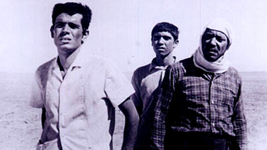 L'image représente trois hommes se tenant dans un paysage désertique. Leurs expressions faciales semblent refléter l'inquiétude ou la tristesse. Le premier homme, à gauche, a les traits anguleux et semble regarder au loin. Le deuxième, au centre, paraît plus jeune et affiche une expression de curiosité ou de perplexité. Le dernier homme, à droite, porte un foulard autour de la tête et a une apparence plus âgée, ce qui pourrait suggérer qu'il a vécu des épreuves. Le fond du paysage est vaste et vide, ce qui accentue l'impression d'isolement et de dureté.