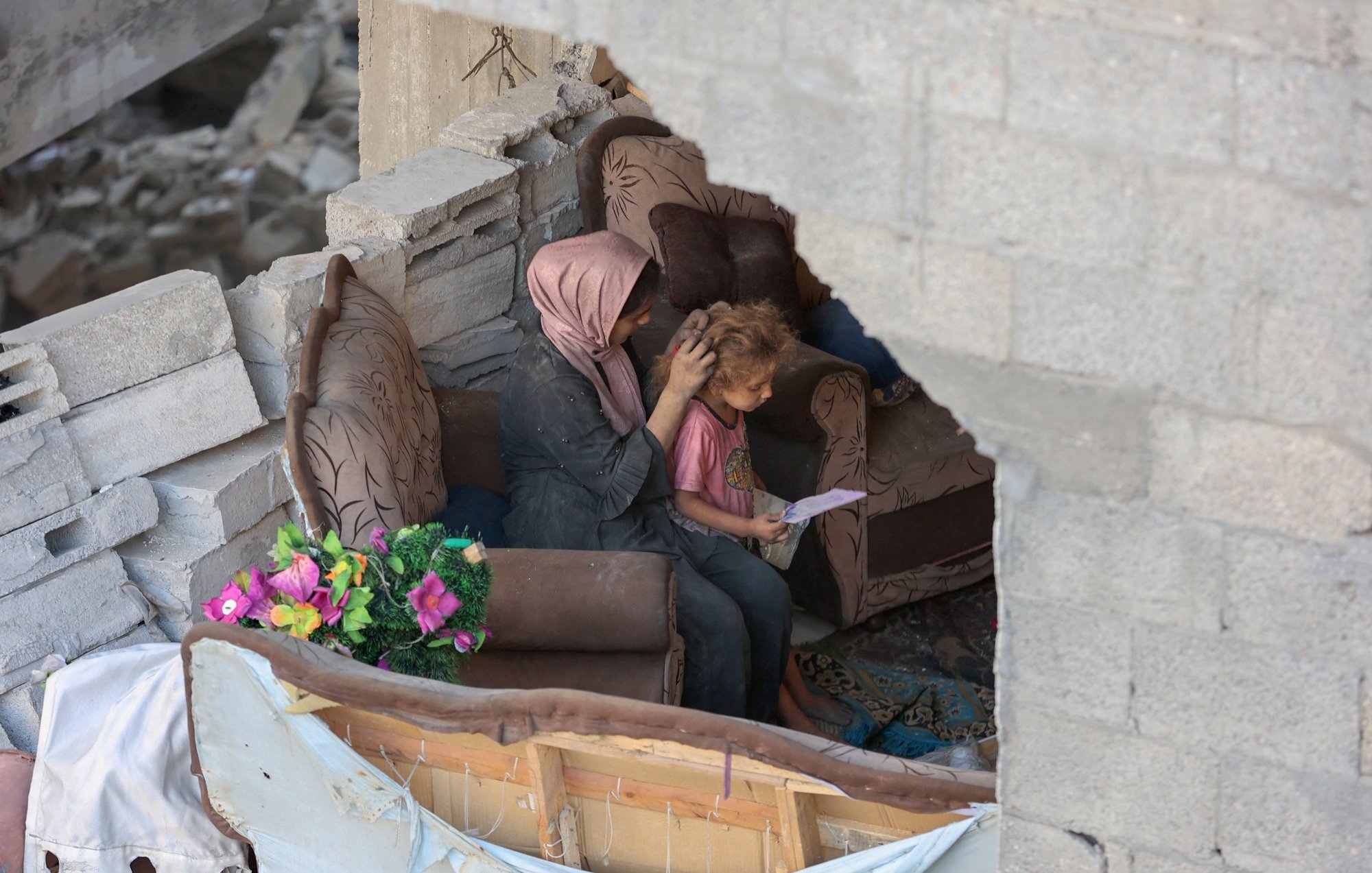 مادری بر روی مبل خراب نشسته و موهای کودک را نوازش می‌کند. در پس‌زمینه، ویرانی مشهود است.