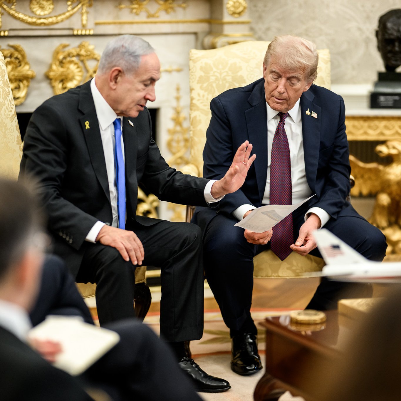 Due uomini in abiti formali discutono seduti su poltrone in un ambiente elegante.