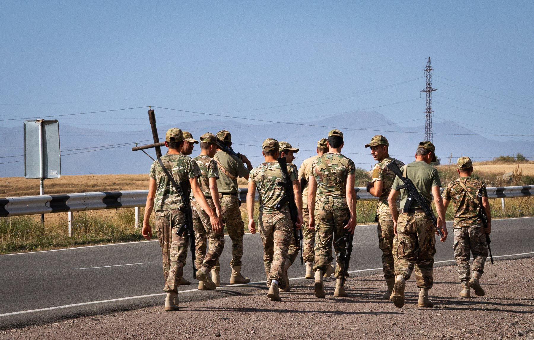 Des soldats marchent en groupe sur une route, avec des montagnes en arrière-plan.