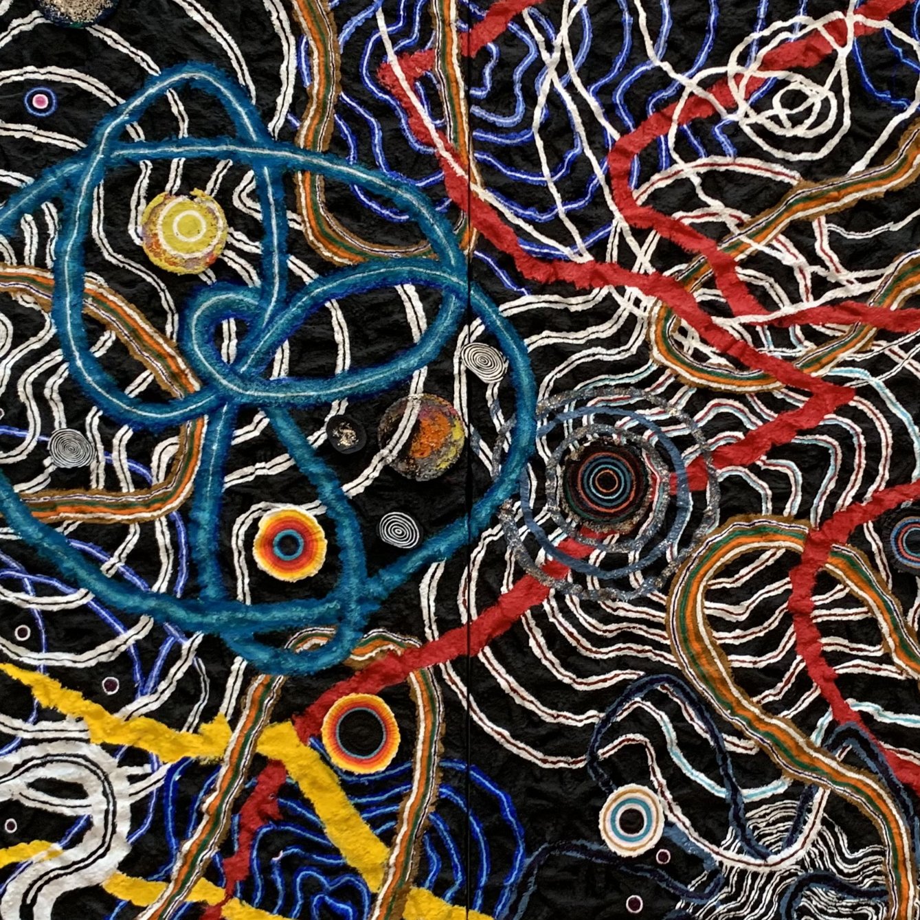 L'image représente un motif complexe et coloré, avec des lignes entrelacées qui dessinent des formes organiques. On y voit des spirales et des cercles de différentes couleurs sur un fond sombre. Les couleurs utilisées, comme le bleu, le jaune et le rouge, contraste avec le noir, créant une impression dynamique et énergique. L'ensemble ressemble à un réseau de connexions, évoquant peut-être des idées de croissance ou d'interconnexion.