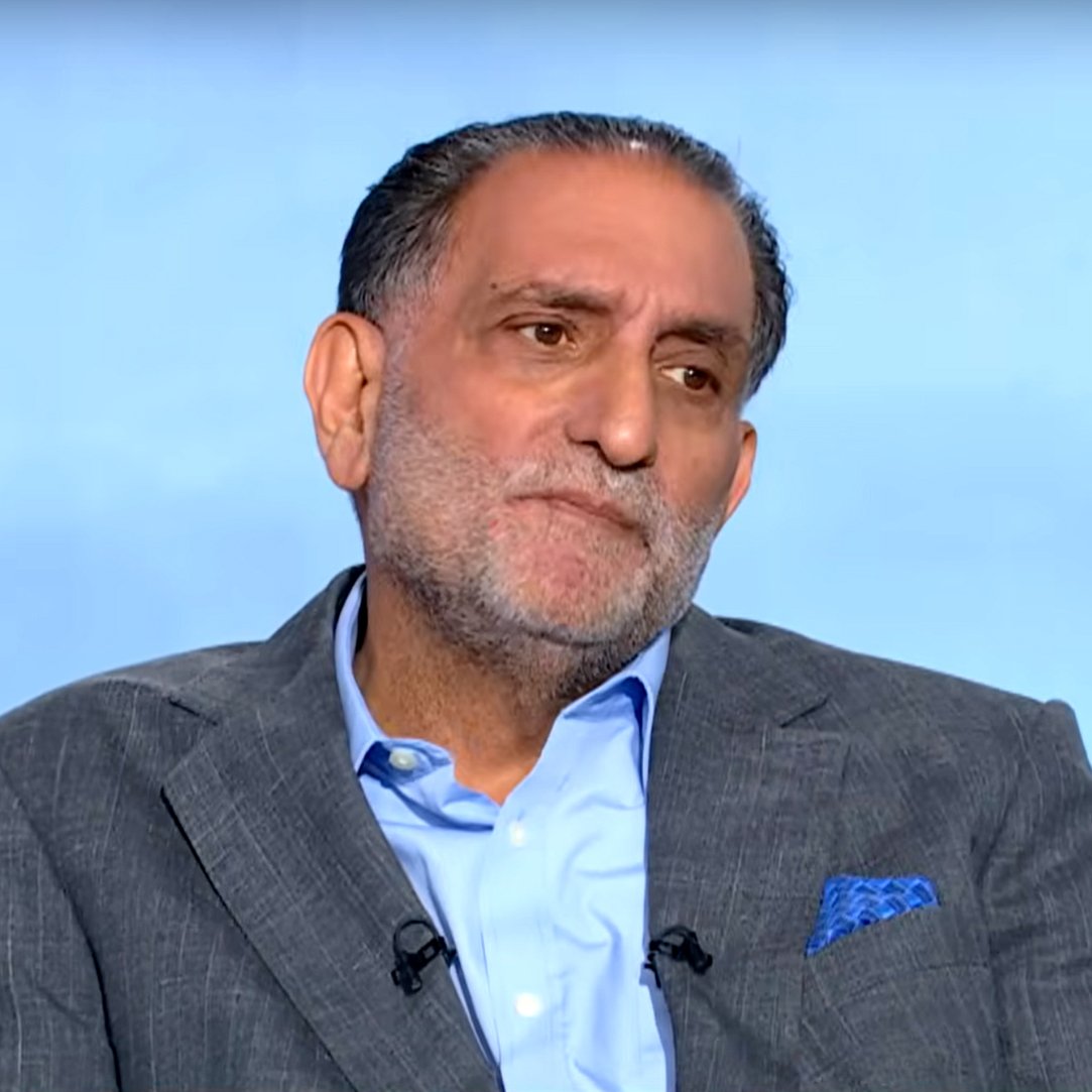 رجل يجلس مرتديًا بدلة رمادية، يبدو عليه التفكير والاهتمام.