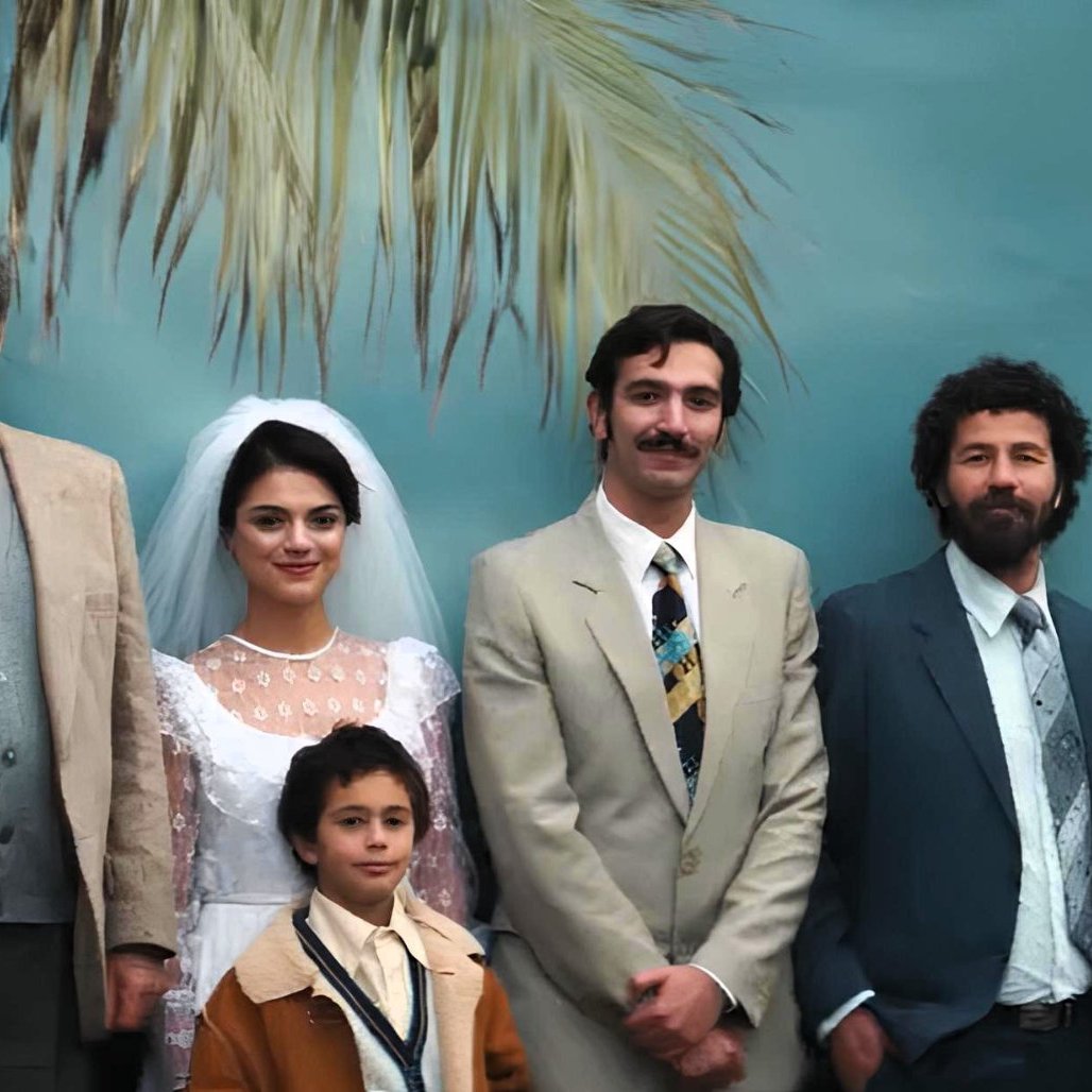 Una famiglia in posa per un matrimonio, sullo sfondo di una palma tropicale.