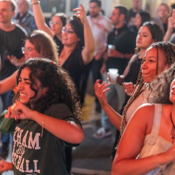 L'image montre un groupe de personnes en train de danser et de profiter d'une ambiance festive. On peut voir des personnes de différents âges, souriantes et s'amusant. Certaines gesticulent au rythme de la musique, tandis que d'autres sont concentrées sur le moment. L'éclairage est chaleureux, ce qui contribue à l'atmosphère joyeuse de l'événement.