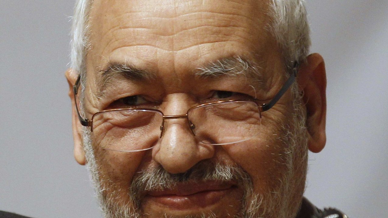 Je ne sais pas qui est cette personne, mais je peux décrire l'image de manière générale. Il s'agit d'un homme d'âge mûr avec des cheveux grisonnants et une barbe. Il porte des lunettes et a un sourire serein. L'arrière-plan semble être flou, ce qui attire l'attention sur lui. Les microphones à proximité suggèrent qu'il pourrait être en train de parler lors d'un événement ou d'une conférence.