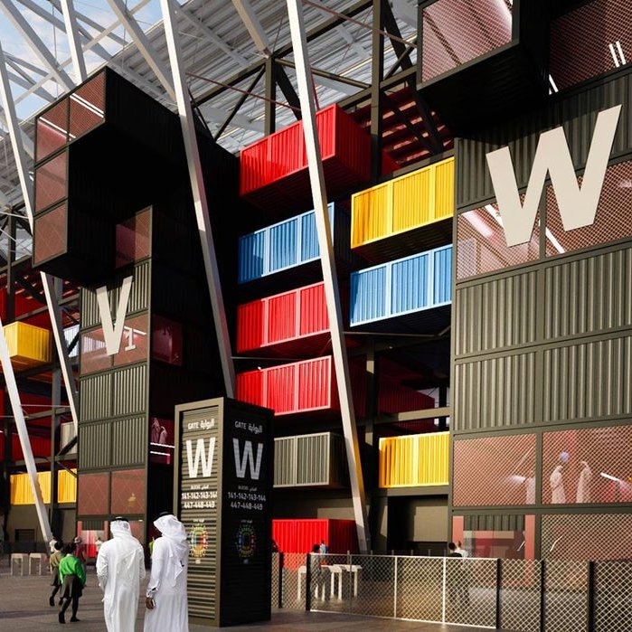 الصورة تظهر تصميمًا عصريًا لمنطقة بجانب ملعب أو منشأة رياضية. يتميز التصميم بألوان زاهية تتضمن الصناديق الملونة بالأسود والأحمر والأصفر والأزرق. هناك أيضًا مدخل واسع مع شعارات واضحة. في الجزء الأمامي، يظهر بعض الأشخاص يرتدون الملابس التقليدية، مما يشير إلى إمكانية وقوع الحدث في منطقة عربية أو إسلامية. السماء تتسم بصبغة رمادية توحي بوقت الغسق.