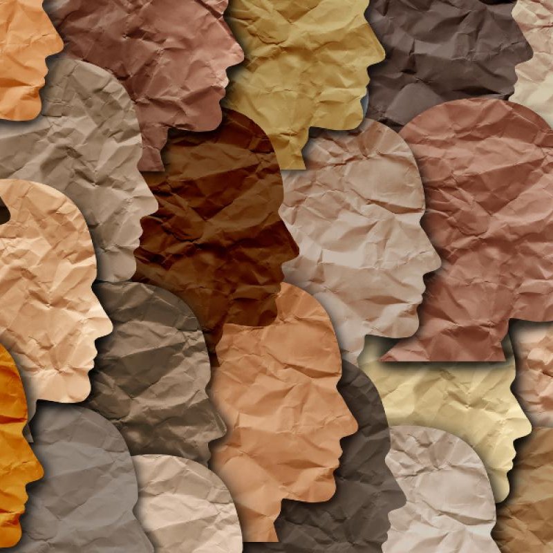 The image features a collage of human profiles created from various shades of crumpled paper. Each silhouette has a different tone, representing a diverse range of skin colors. The overlapping and varied textures of the paper give depth and interest to the composition, highlighting themes of diversity and inclusion. The overall effect is a harmonious blend of shapes and colors.