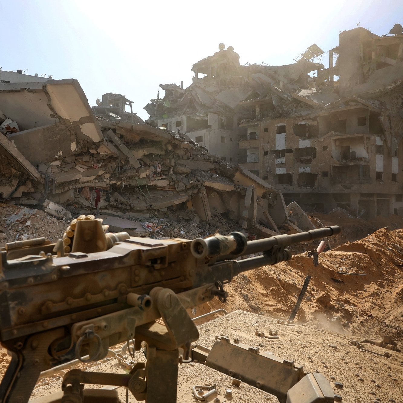Un fusil pointé vers des bâtiments en ruines, sous un ciel lumineux.