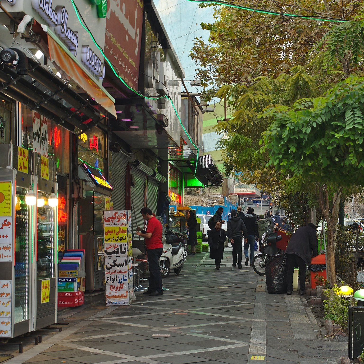 A bustling street lined with shops, colorful signs, and people walking along the pavement.