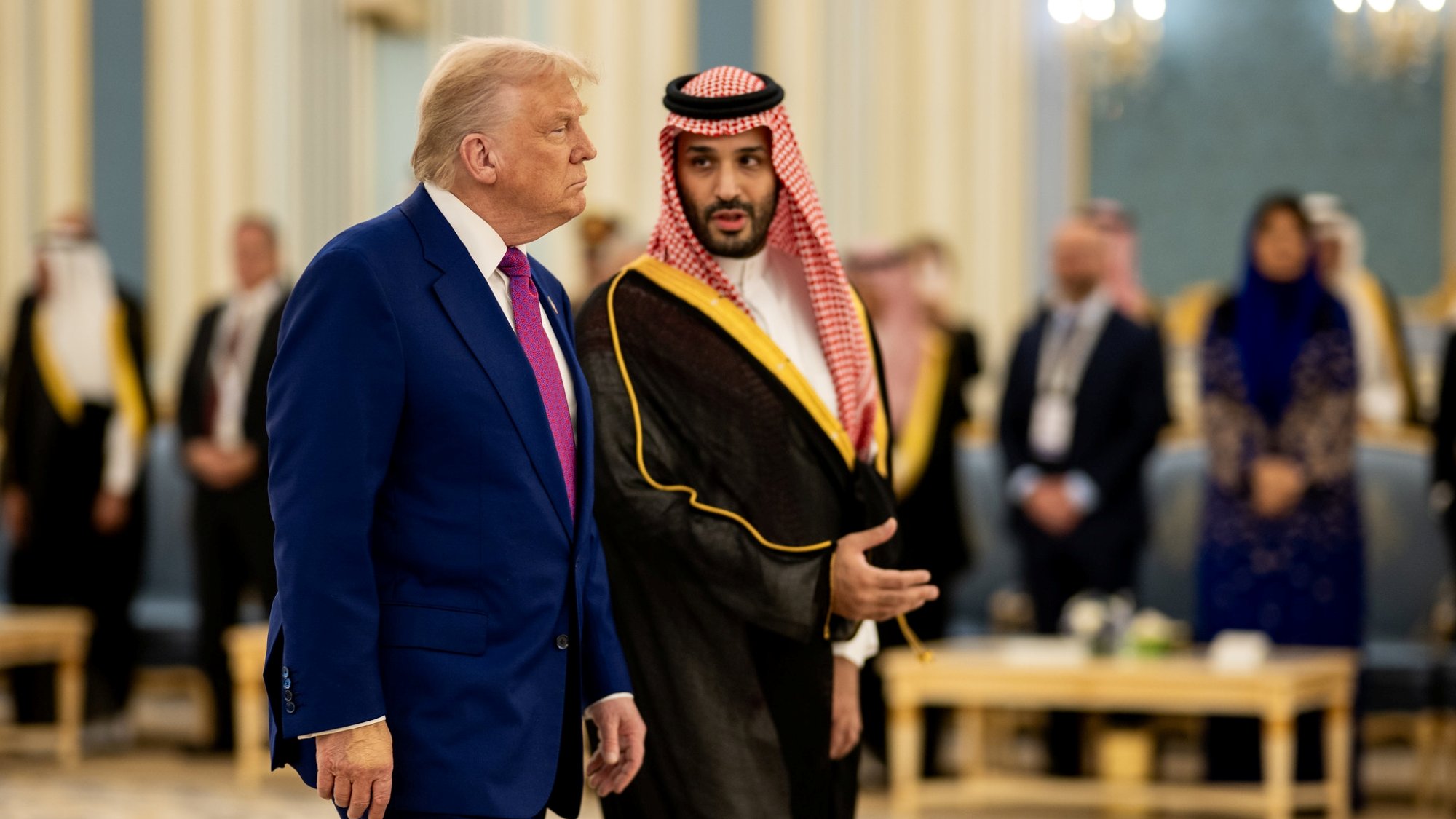 Deux hommes en costume, l'un américain et l'autre saoudien, discutent dans un hall élégant.