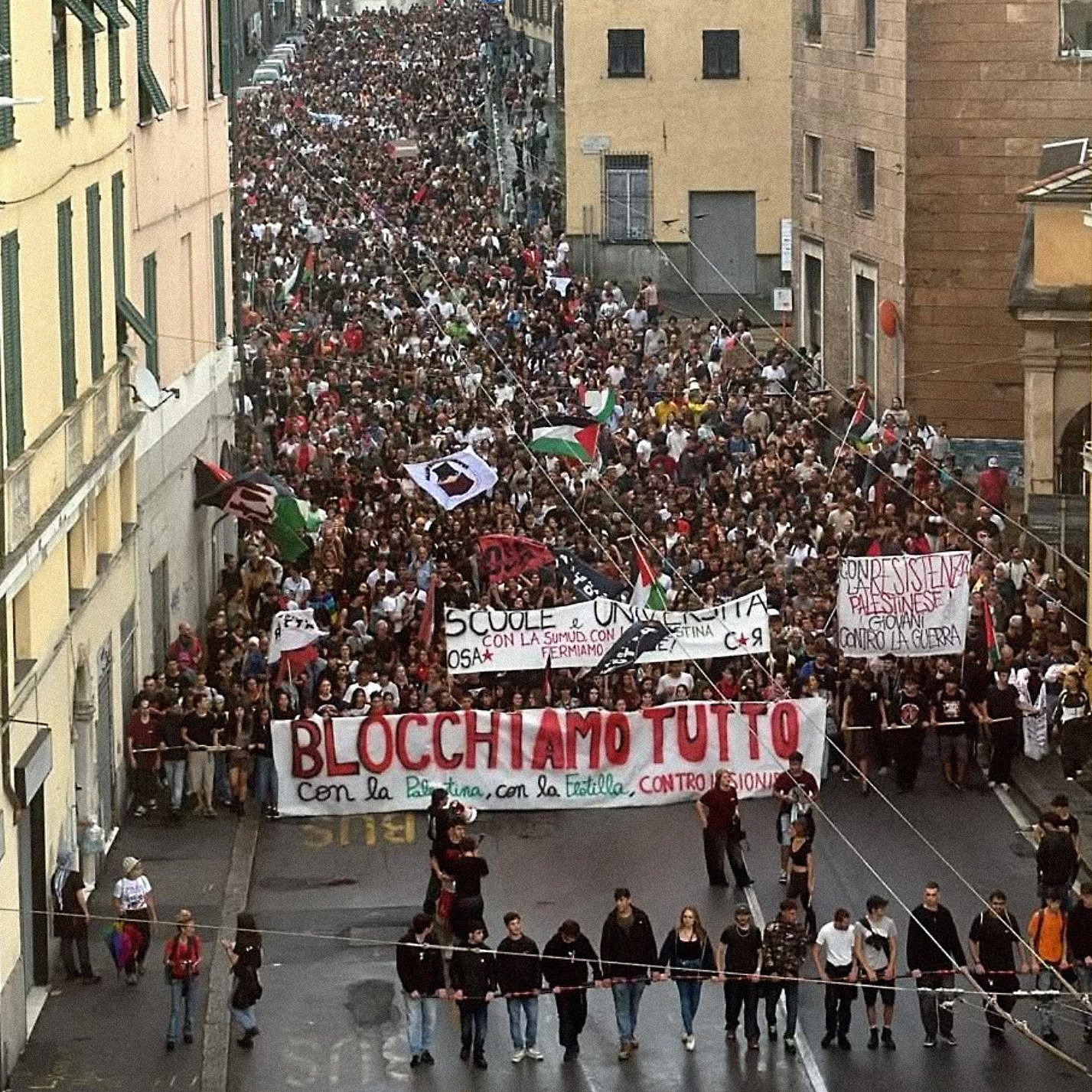 Una grande manifestazione con moltissime persone che sfilano, portando striscioni.