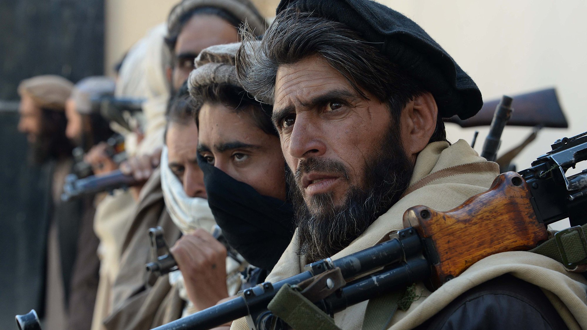 این تصویر گروهی از مردان مسلح را نشان می‌دهد که در یک وضعیت آماده‌باش قرار دارند. آنها لباس‌های سنتی دارند و بعضی از آن‌ها صورت خود را با پارچه پوشانده‌اند. سلاح‌هایشان بر دوششان قرار دارد و تمرکز و جدیت آن‌ها در چهره‌شان مشهود است. زمینه فقط به صورت محو دیده می‌شود و توجه بیشتر به افراد معطوف است.