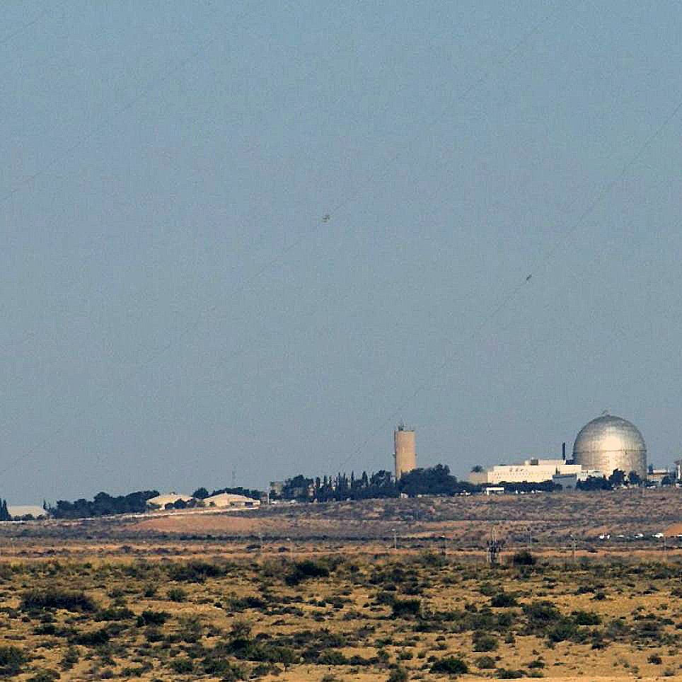 الصورة تظهر مشهداً لبيئة طبيعية صحراوية مع مبانٍ تظهر في الخلفية. يبدو أن هناك مرفقاً يحتوي على قبة كبيرة، ومن المحتمل أن يكون هذا المرفق مركزاً علمياً أو مفاعلاً نووياً. كما يُلاحظ وجود أعمدة مدخنة تشير إلى أنشطة صناعية. السماء صافية واللون العام للصورة يميل إلى الألوان الترابية.