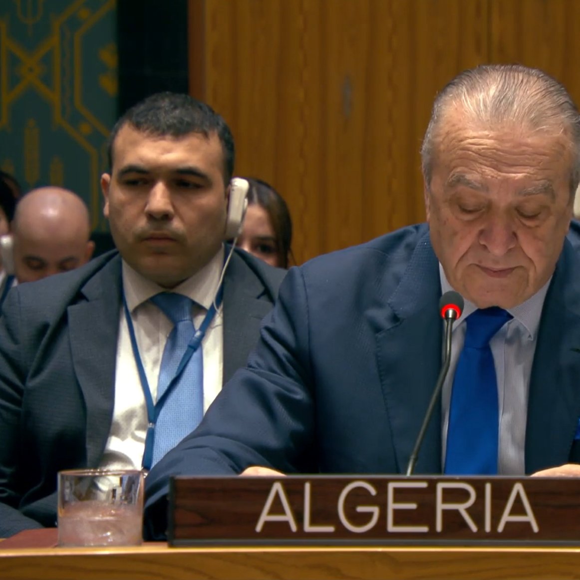 A man in a suit speaks at a podium labeled "Algeria" in a formal setting with delegates behind him.