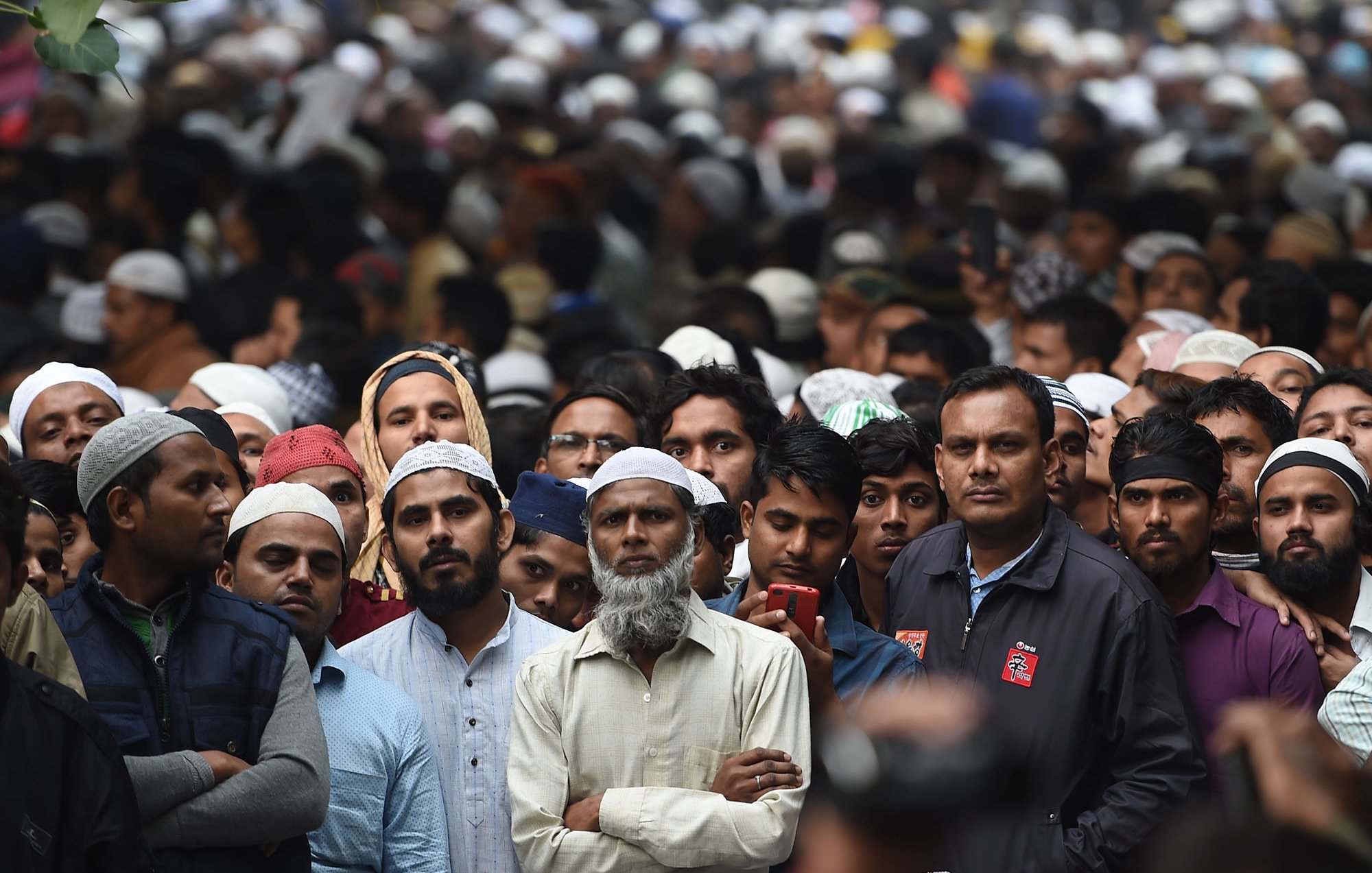 La imagen muestra una multitud de personas, muchas de las cuales llevan puestos kufis o tapones. La mayoría de las personas parecen estar prestando atención a algo en frente de ellos, algunos lucen serios y concentrados. Hay una gran diversidad de edades entre los asistentes y la atmósfera parece de expectativa. El fondo está lleno de más personas, lo que indica que es una reunión o evento masivo.