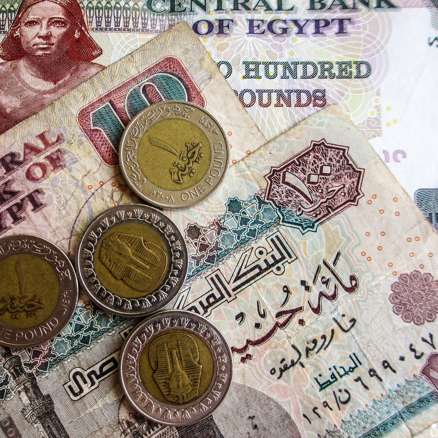 در این تصویر، تعدادی پول نقد مصری به نمایش گذاشته شده است. شامل یک اسکناس ۲۰۰ پوندی و یک اسکناس ۱۰ پوندی که در پس‌زمینه دیده می‌شود. همچنین چهار سکه یک پوندی روی اسکناس‌ها قرار دارد. طراحی اسکناس‌ها و سکه‌ها حاوی نقوش و نوشته‌هایی به زبان عربی است که بیانگر هویت بانک مرکزی مصر و ارزش پول‌ها می‌باشد. رنگ‌های مختلف اسکناس‌ها و سکه‌ها به وضوح قابل مشاهده است.