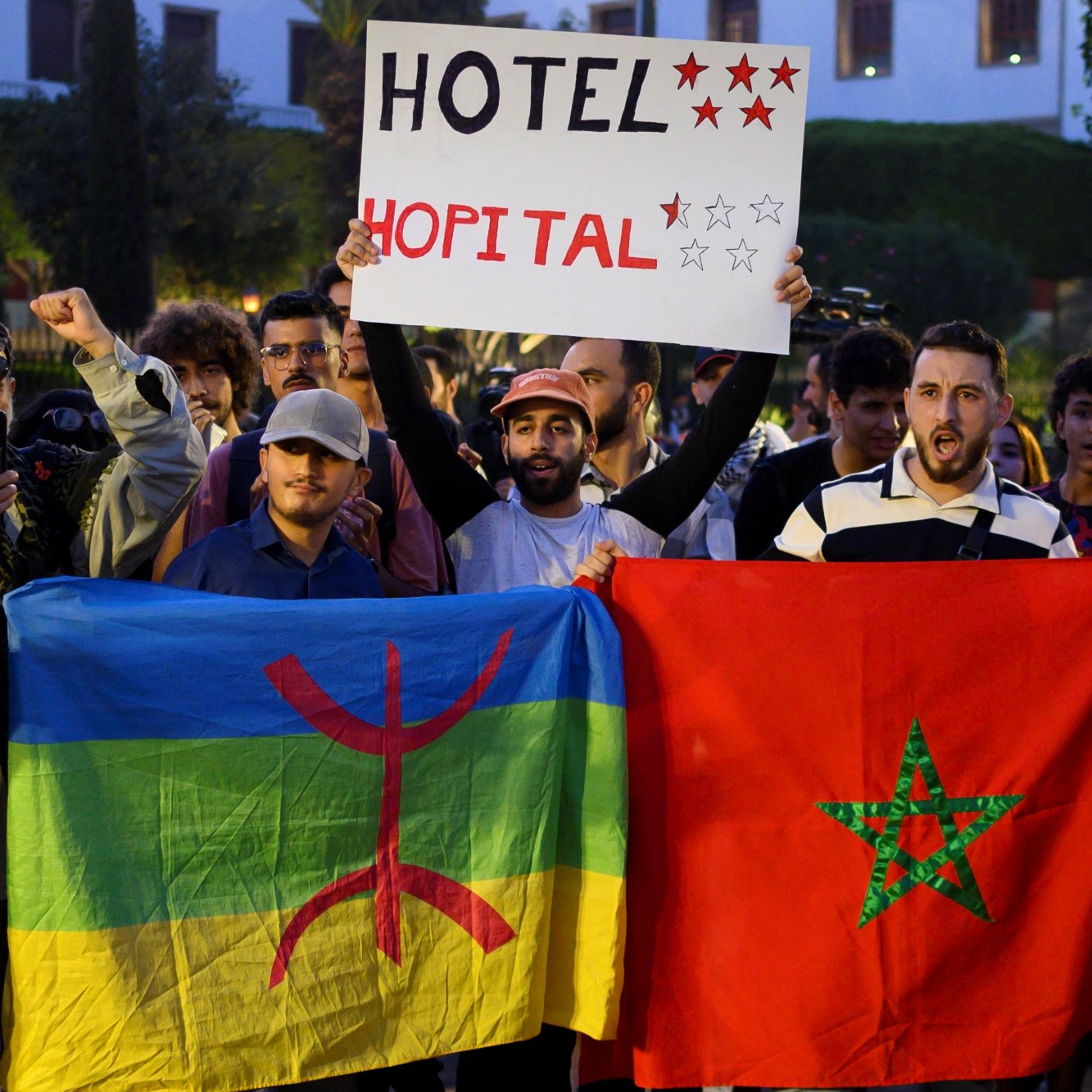 Manifestation avec des drapeaux marocains et amazigh, pancarte pour un hôtel.