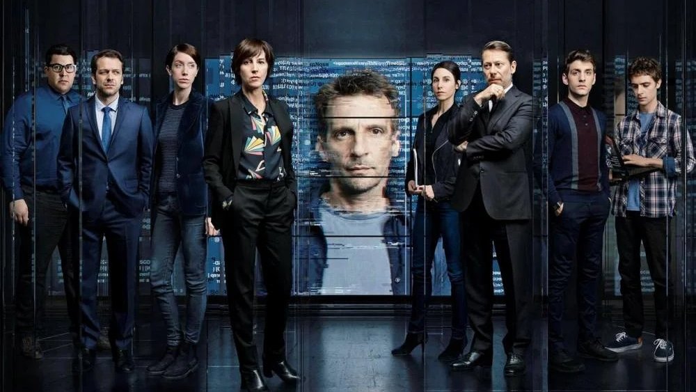 L'image présente un groupe de personnes stylisées, probablement des acteurs, se tenant debout dans un environnement sombre et futuriste. Au centre, un écran numérique affiche le visage d'un homme, tandis que les membres du groupe adoptent des poses sérieuses. Ils portent des vêtements formels et décontractés, suggérant une ambiance à la fois professionnelle et tendue. L'ensemble de l'image évoque un thème lié à la technologie ou aux enquêtes, avec une atmosphère de mystère.