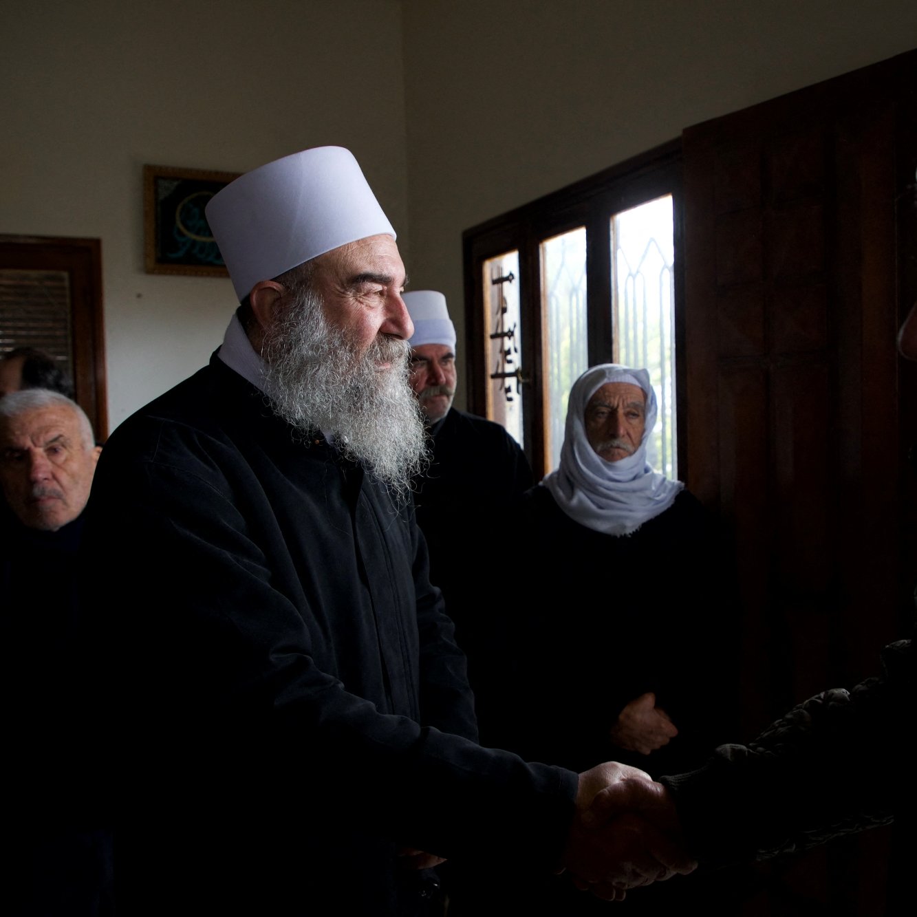 Des hommes en vêtements sombres se serrent la main dans une pièce avec des fenêtres.