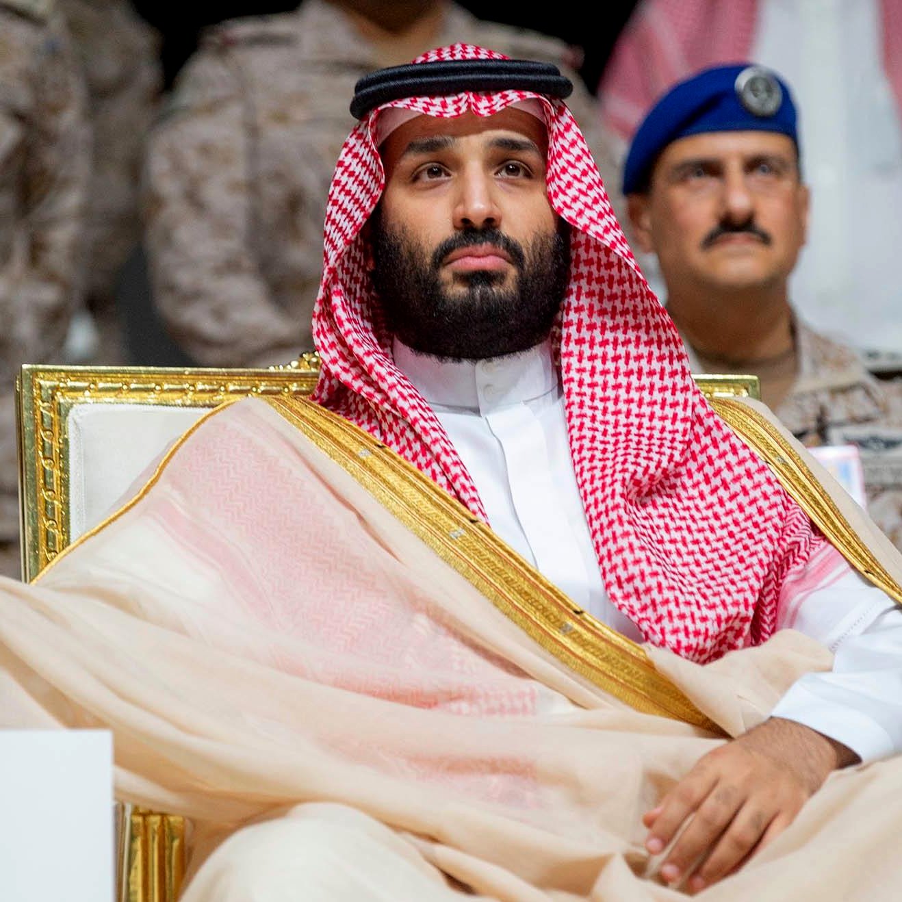 Un uomo in abiti tradizionali arabi, seduto su una sedia dorata, con uno sguardo serio.