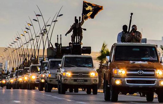 L'image montre une ligne de véhicules tout-terrain circulant sur une route. Certains des véhicules sont équipés d'armes lourdes et portent des drapeaux. Le ciel est partiellement nuageux, ce qui donne une ambiance dramatique à la scène. Des soldats sont visibles à bord des camions, suggérant une présence militaire importante. Des éléments urbains, comme des lampadaires et des bâtiments, sont également présents en arrière-plan.