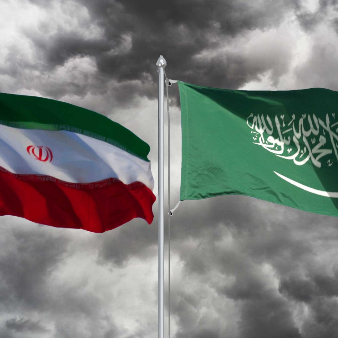 Nell'immagine sono visibili due bandiere: quella dell'Iran a sinistra e quella dell'Arabia Saudita a destra. Entrambe le bandiere sono sovrapposte a uno sfondo scuro e nuvoloso, creando un contrasto suggestivo. La bandiera iraniana è composta da bande orizzontali di verde, bianco e rosso, con lo stemma nazionale al centro. La bandiera saudita è verde, con la scritta in arabo e una spada bianca. L'insieme trasmette una sensazione di tensione e rivalità tra i due paesi.