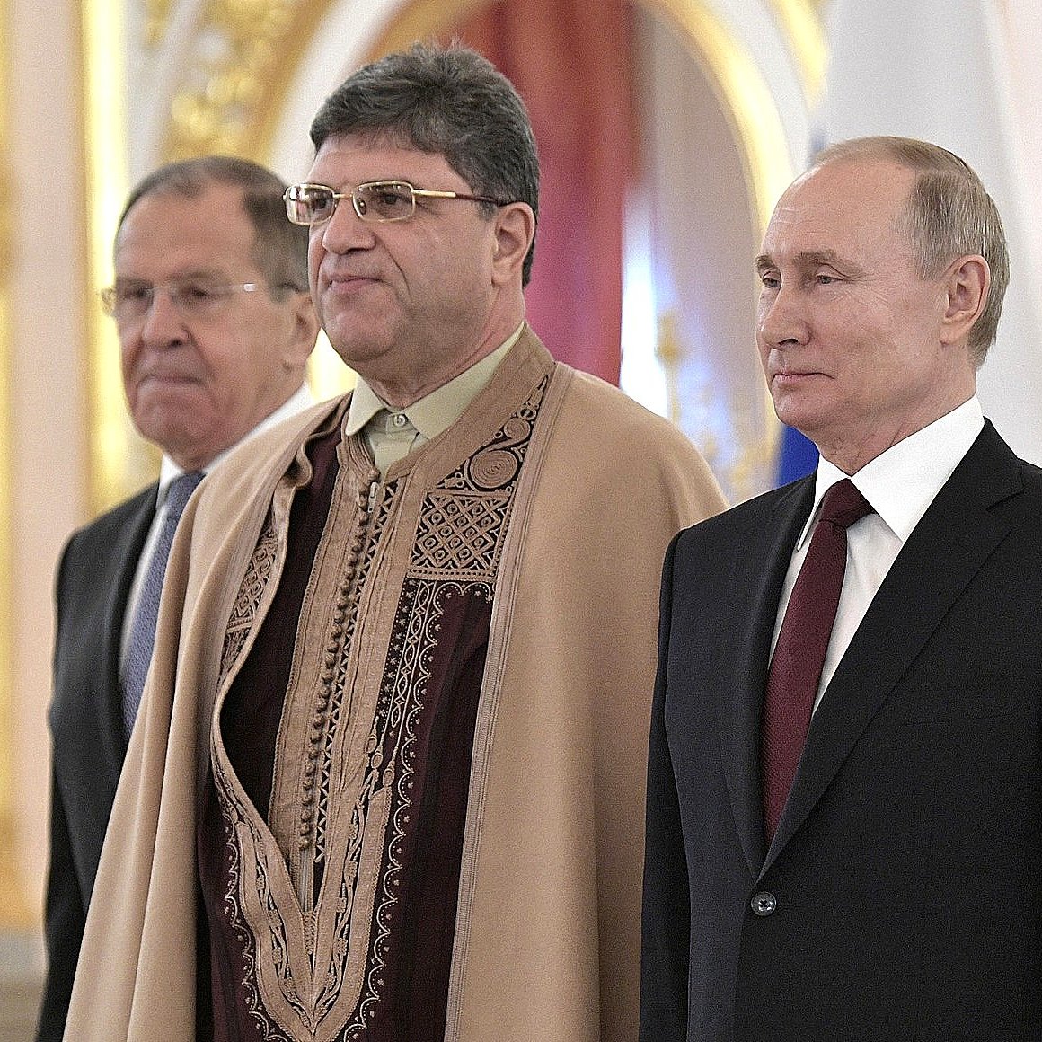 تظهر في الصورة مجموعة من الأشخاص يقفون في مكان رسمي. في الخلفية، يمكن رؤية زخارف وقاعات ذات تصميم راقٍ. يبدو أن الأفراد يرتدون ملابس رسمية، حيث يتواجد شخص يحمل زيًا تقليديًا مميزًا. يُظهر المشهد جوًا من الاحتفال أو التقدير.