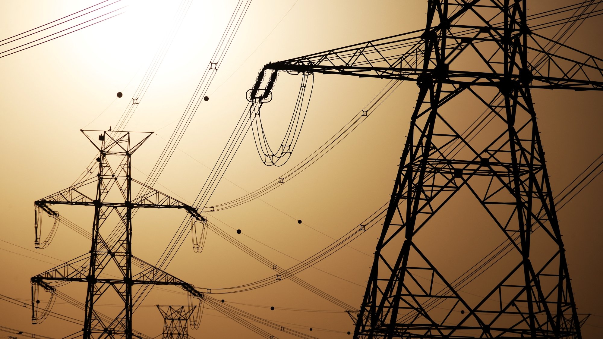 Silhouettes de pylônes électriques contre un ciel orangé.