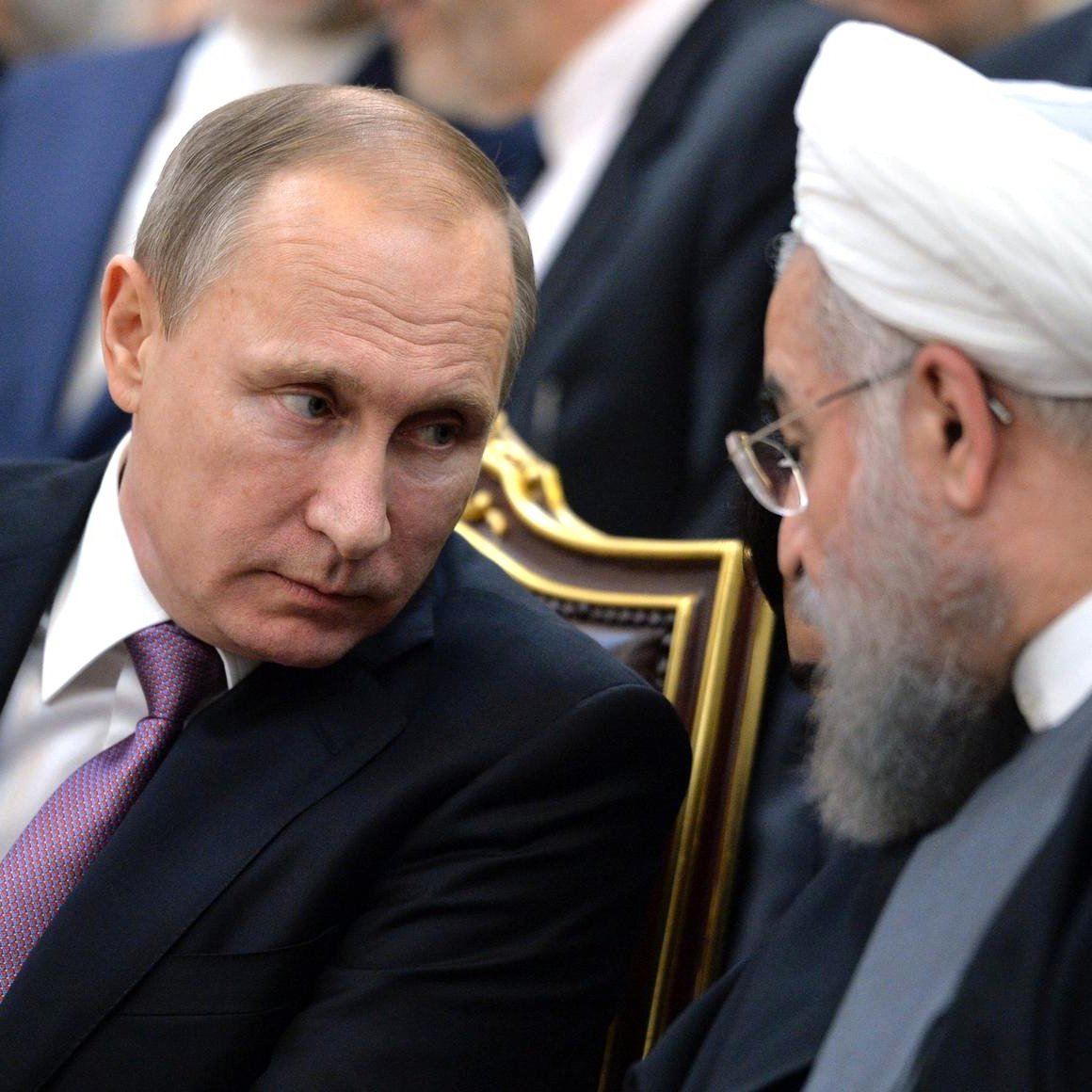 L'image montre deux hommes en train de discuter, assis côte à côte. L'un porte un costume noir avec une cravate et a un regard sérieux, tandis que l'autre est en tenue traditionnelle avec un turban et une barbe. Leurs expressions reflètent une conversation attentive. L'environnement est formel, suggérant un contexte politique ou diplomatique.