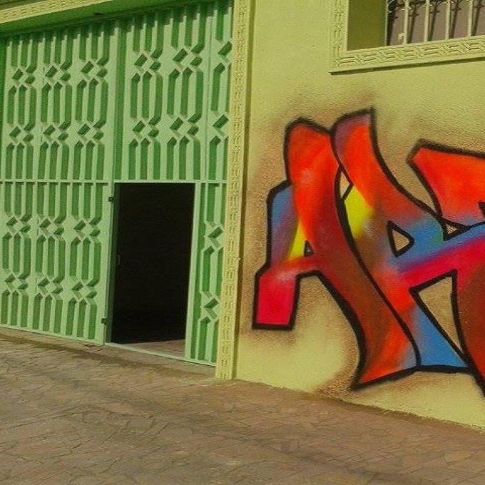 L'image montre un mur coloré peint en graffiti, où le mot "ART" est mis en avant. Les lettres sont stylisées avec des couleurs vives, notamment du rouge, du jaune, du orange et du bleu, se détachant sur un fond de mur vert. À côté du graffiti, on aperçoit une porte ouverte, ajoutant du caractère à l'ensemble de la scène. Le style du graffiti donne une impression dynamique et artistique à cet espace.