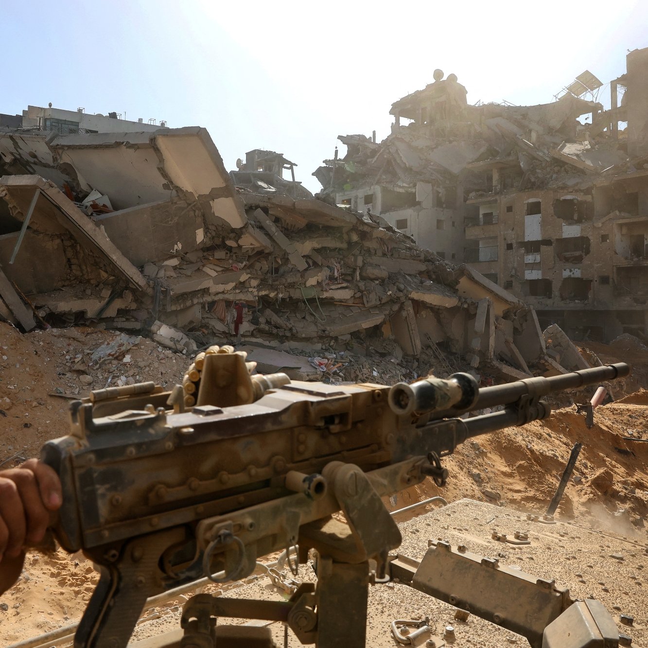 Una zona devastata, edifici crollati e un fucile appoggiato su un treppiede.