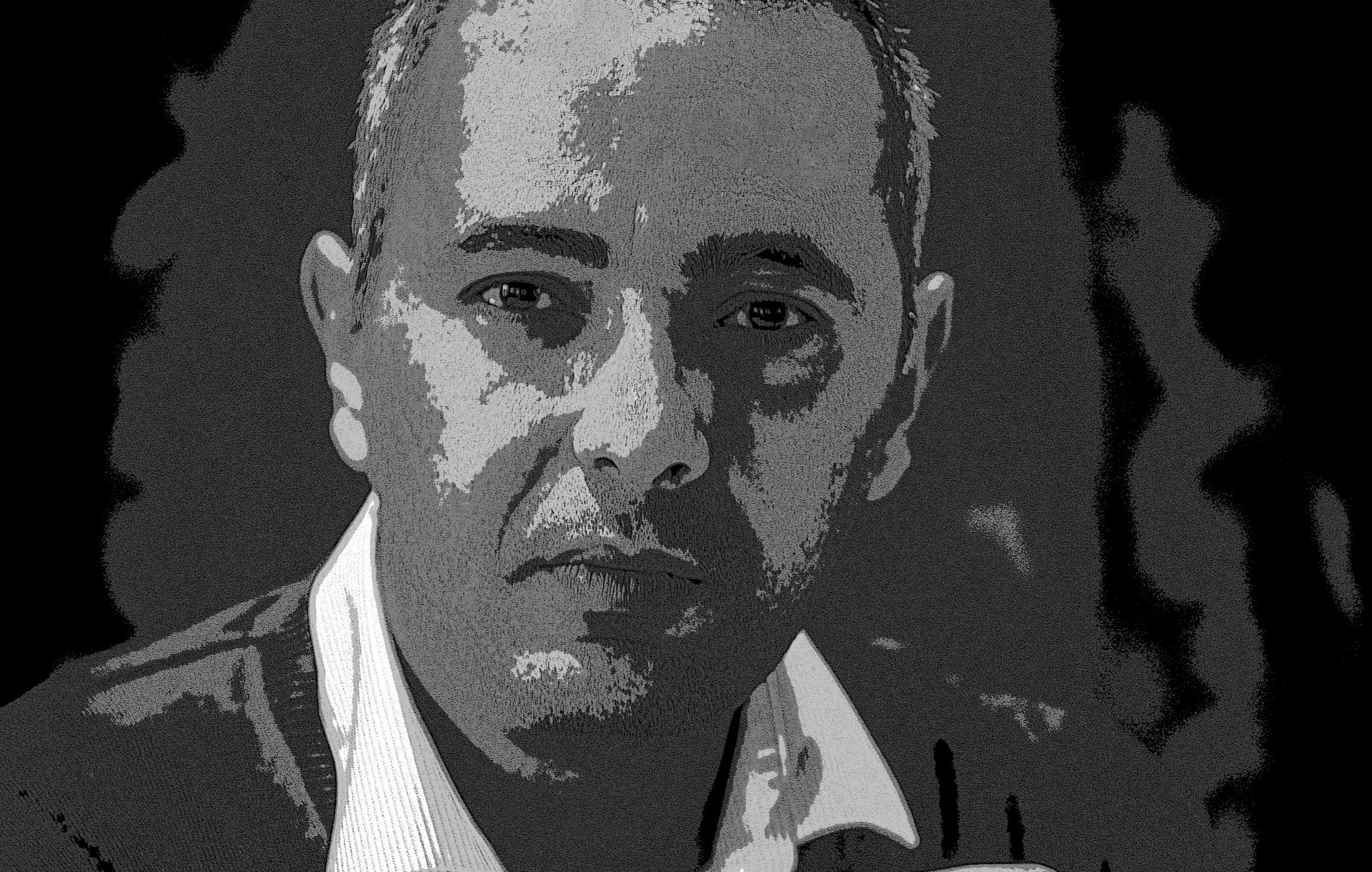 L'image montre un homme avec une expression réfléchie. Il a les cheveux courts et porte un pull. Ses mains sont croisées devant lui. Le fond est sombre, ce qui met en avant son visage. L'éclairage accentue ses traits et donne une atmosphère sérieuse à la photo.