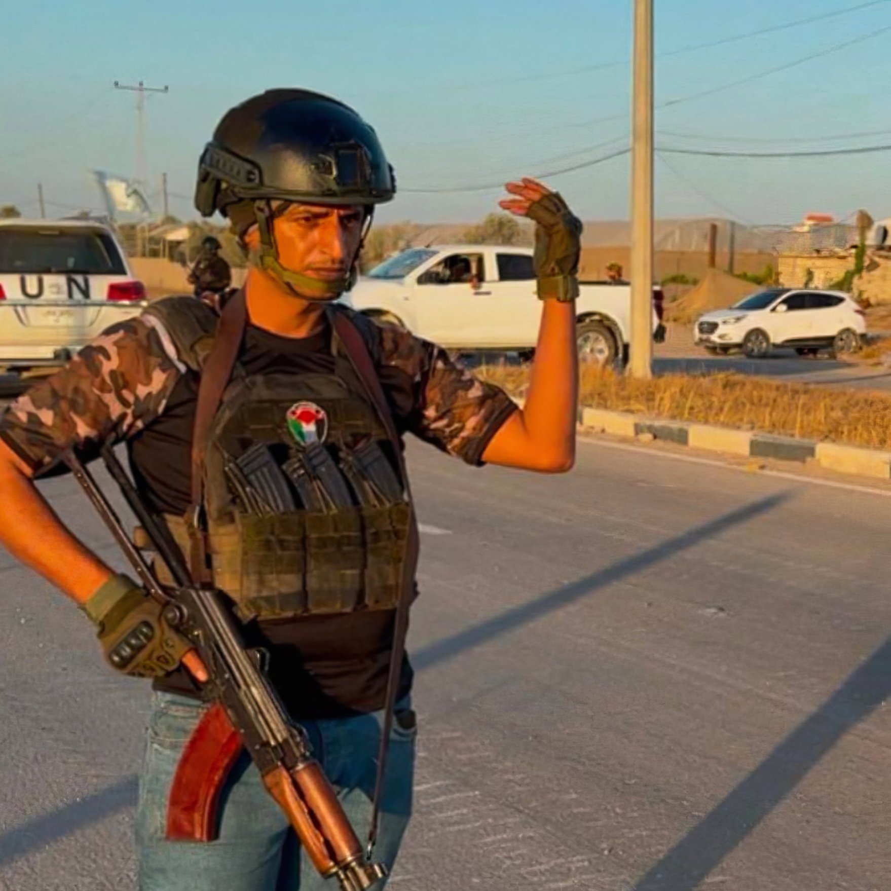 یک مرد با کلاه ایمنی و جلیقه ضد گلوله، اسلحه کلاشنیکف را در دست دارد و در خیابان ایستاده است.