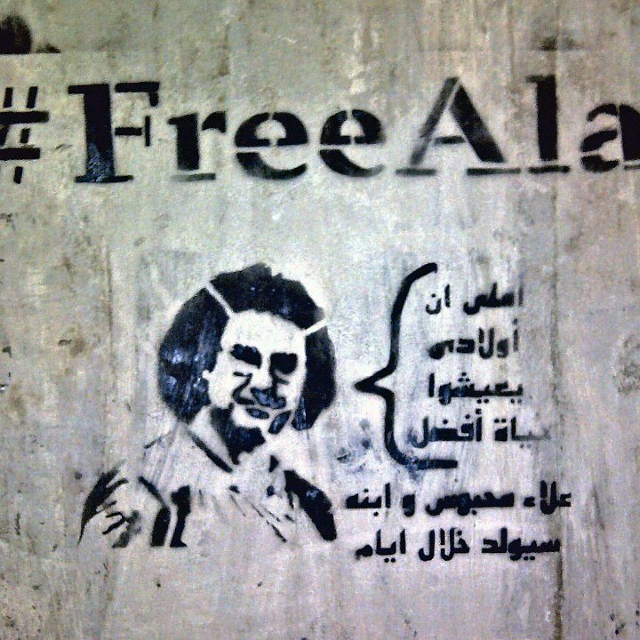 L'image présente un graffiti sur un mur. Le texte "#FreeAlaa" est inscrit en haut, accompagnant un dessin stylisé d'une personne. En dessous, il y a une citation en arabe qui semble évoquer des thèmes de liberté ou de résistance. L'ensemble donne une impression de soutien à une cause ou un individu en particulier, en soulignant la lutte pour la liberté d'expression.