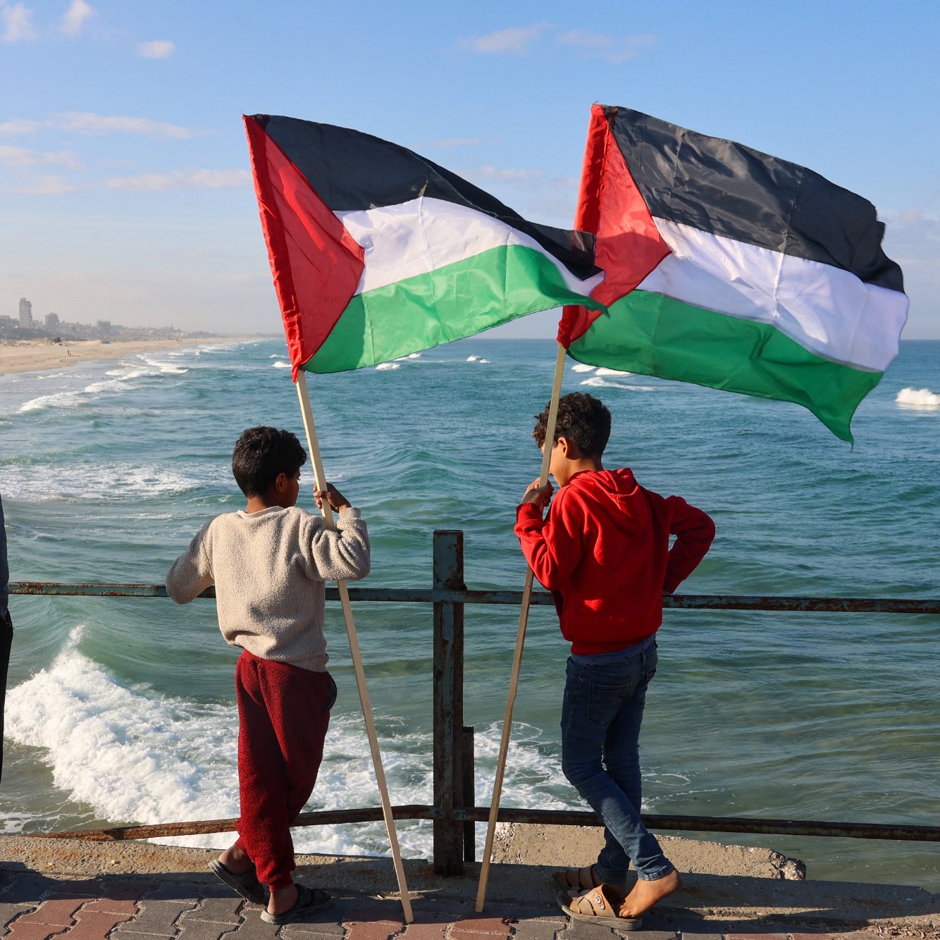 در این تصویر، سه کودک در کنار دریا ایستاده‌اند و به سمت امواج دریا نگاه می‌کنند. یکی از کودکان پرچم فلسطین را در دست دارد و دو نفر دیگر نیز در حال نظارت بر صحنه هستند. لباس‌های آن‌ها متنوع است و در پس‌زمینه می‌توان نمایی از سواحل و ساختمان‌های شهری را مشاهده کرد. آسمان آبی و ابرهای کمی در بالای تصویر وجود دارد که حال و هوای دلپذیری را به تصویر می‌دهد.