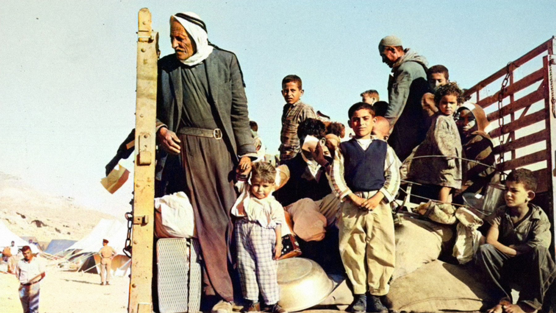 Gruppo di persone, molte famiglie e bambini, su un camion in un contesto di crisi.