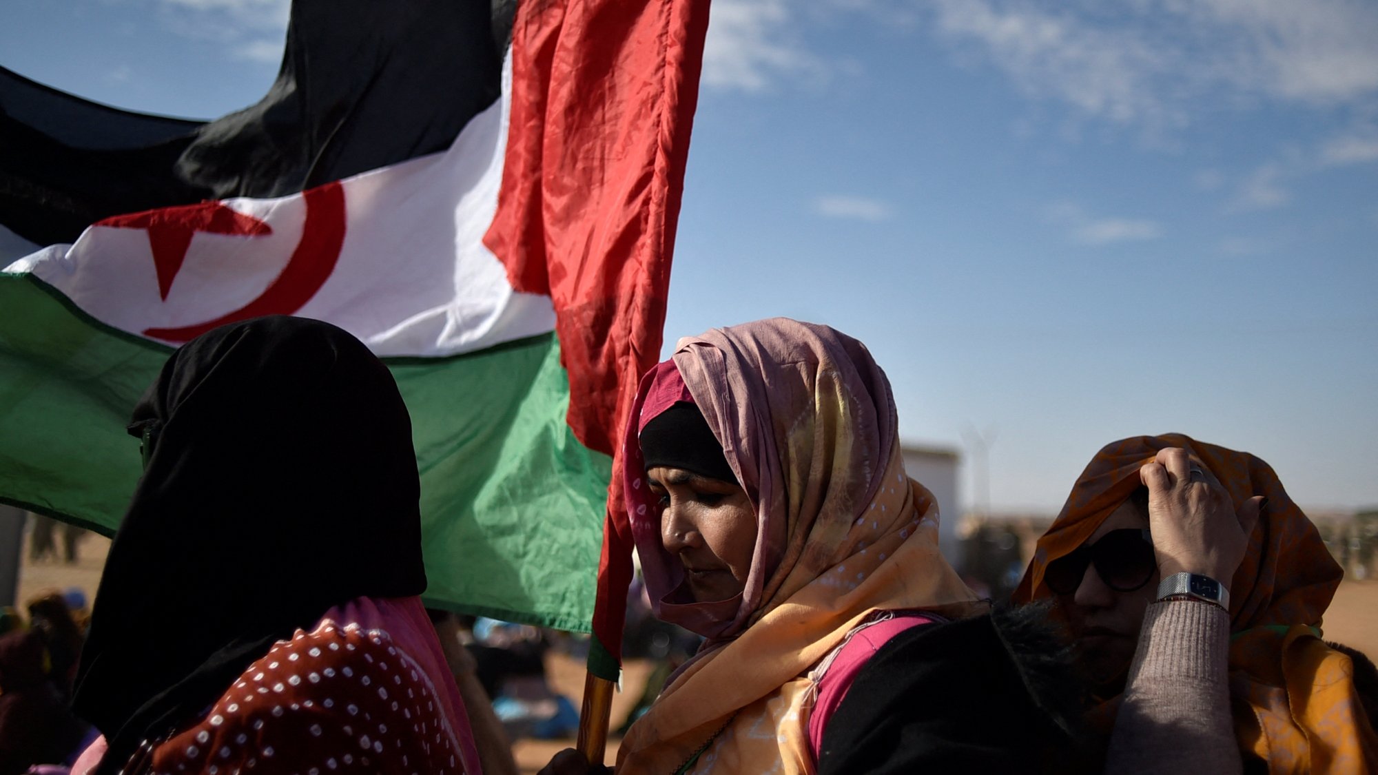 Des femmes portant une écharpe colorée et une grande bannière. Ciel dégagé en arrière-plan.